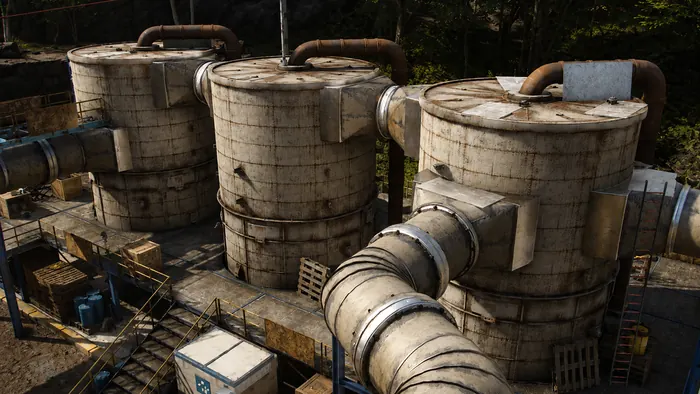 Rusted refinery tanks and pipework kit on a paved yard