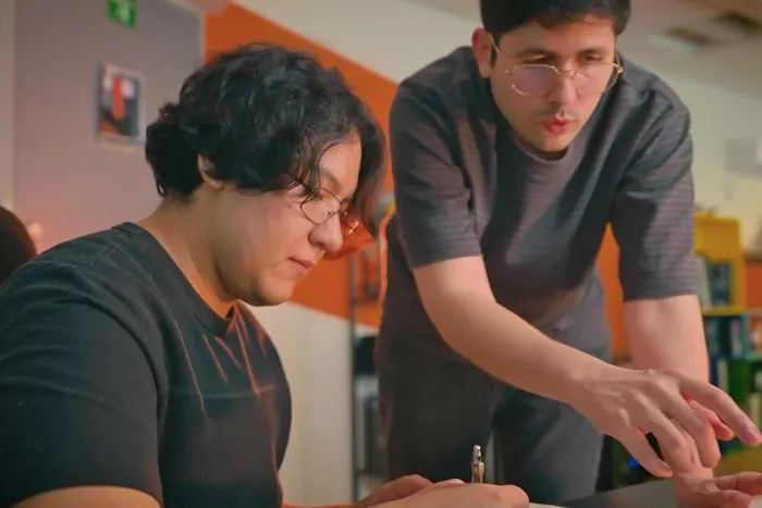 A CGBOT artist sketching at his desk while a lead leans in to review the work