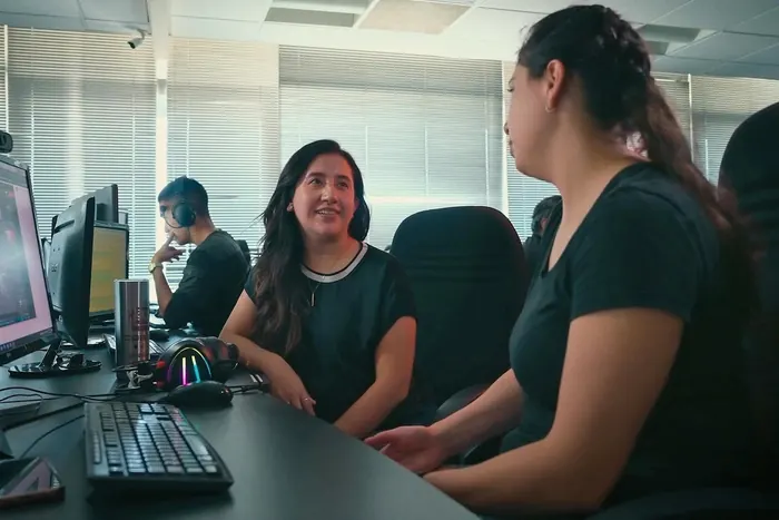 Two CGBOT artists chatting at their workstations while a teammate works with headphones on behind them